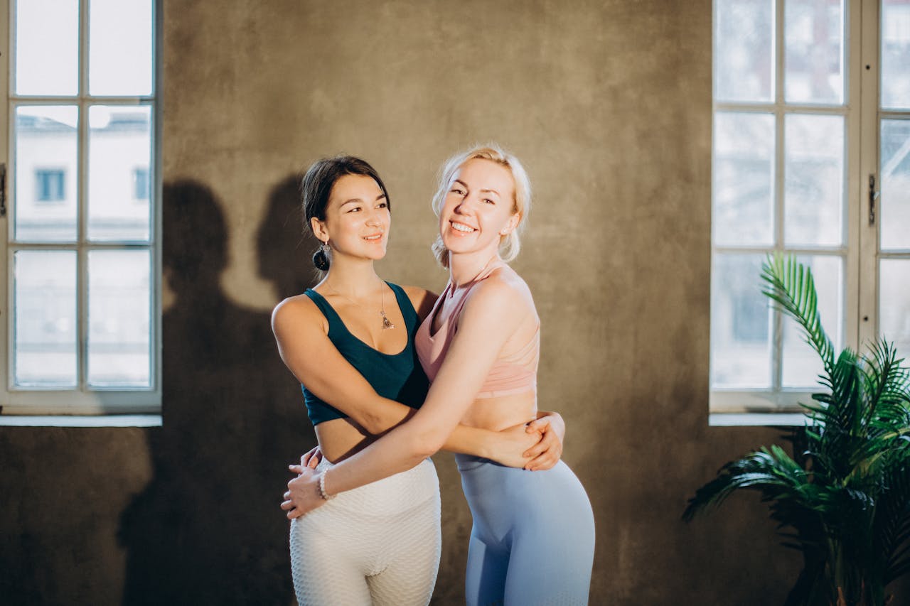 Two women in sportswear, embracing with smiles in a sunlit room.